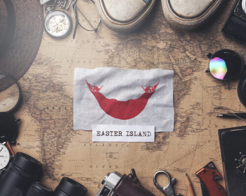 Bandera de la Isla de Pascua entre los accesorios de viaje en un mapa antiguo. Fotografía cenital.